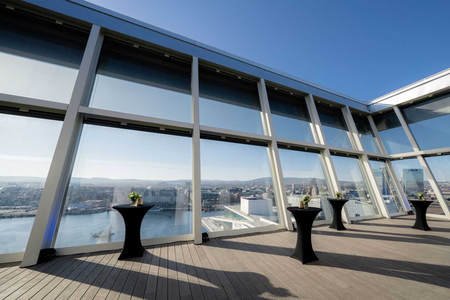 The Sky Room's rooftop terrace with small black tables. Blue skies, the city and the fjord below. 