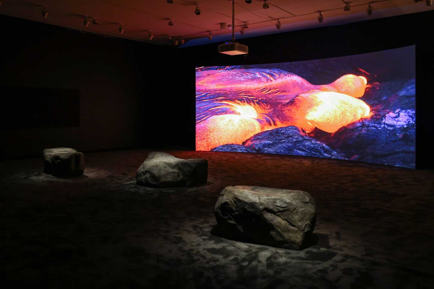 Mørkt rom med storskjerm som viser video og steiner til å sitte på i forkant