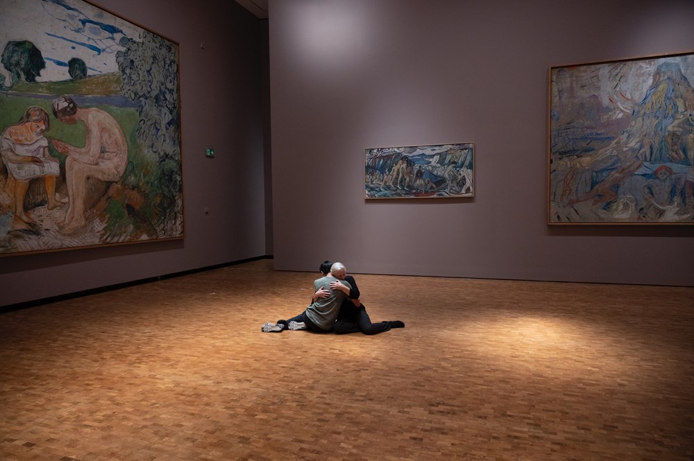 To dansere omfavner hverandre sittende på gulvet omgitt av Edvard Munchs monumentale verk. 